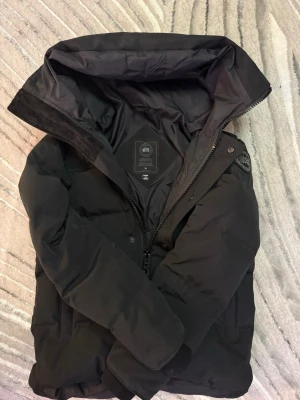 SVART MACMILLAN Canada Goose - Säljer en svart dunjacka från Canada Goose. En dunjacka i mycket bra skick. Otroligt varm och perfekt för kalla vinterdagar. Stilren, slitstark.  Inga skador alls och passar till en bra kylig dag. 