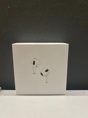 Apple AirPods med Lightning-laddning - Säljer ett par vita Apple AirPods 3 med Lightning-laddningsetui. Trådlösa in-ear hörlurar i stilren design, tillverkade i plast. Perfekta för musik, samtal och vardagsbruk. Kommer i originalförpackning.