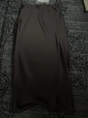 Brun satinlångkjol från Neo Noir - Snygg brun långkjol från Neo Noir i glansigt satinmaterial. Kjolen har en rak och enkel siluett som ger en stilren look. Perfekt att matcha med både stickade tröjor och toppar för en trendig outfit.