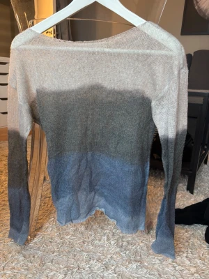 Stickad tröja i beige, grå och blå - Säljer en tunn stickad tröja från Pull&Bear i storlek M. Tröjan har ett snyggt färgblocksmönster i beige, grått och blått. Långärmad modell med rund halsringning och avslappnad passform