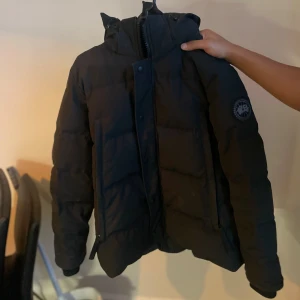 Äkta Svart blacklabel parka jacka från Canada Goose - Säljer en svart blacklabel parka jacka från Canada Goose med huva. Jackan har dragkedja och knappar framtill, samt två sidofickor. Perfekt för kalla dagar med sin tjocka och vadderade design. Passar dig som gillar stilren och funktionell vinterjacka. Jackan kommer med kvitto sertifikat samt boxen