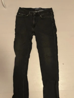 Svarta slim fit jeans - Säljer ett par svarta slim fit jeans med klassisk femficksdesign och snygga slitningar. Jeansen har normal midja och dragkedja med knapp. Perfekta till en avslappnad streetstil och passar till det mesta i garderoben. Dressman