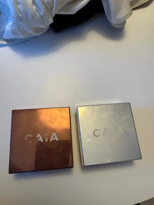 CAIA Loose Glow Bronzer Florence - Säljer en CAIA Loose Glow Bronzer i nyansen Florence. Kommer i en snygg, fyrkantig förpackning i kopparfärg med CAIA-logga. Produkten är ett löspuder som ger en varm, solkysst look och har en glow-finish. Perfekt för att framhäva ansiktets konturer.
