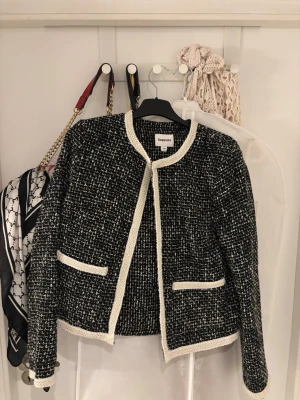 Svartvit tweed cardigan från Kappahl - Stilren svartvit tweed cardiganjacka från Kappahl med öppen front och dekorativa vita kanter. Skit snygg men har tyvärr inte använts nångång av mig! Den är i storlek 38 men är mindre i modellen och sitter som xs/s.