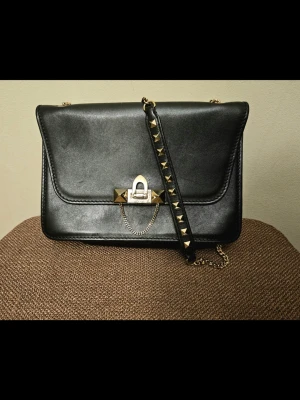 Svart Valentino Garavani Rockstud Demi-Lune Axelväska - Autentisk Valentino Garavani Rockstud Demi-Lune Axelväska – Svart & Guld  Limiterad upplaga av Valentino Rockstud Demi-Lune axelväska i svart läder med gulddetaljer. Ikonisk halvmåneformad silhuett med signaturpyramidnitar. Inkluderar original Valentino-presentask och äkthetskort. Digital kopia av originalkvitto från Valentino Saint-Tropez (09/09/2017, 1 400 €). Utmärkt skick. Tidlös lyxklassiker till ett bra pris.