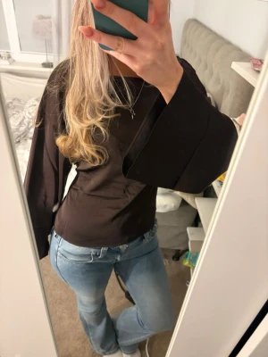 Mörkbrun  omlottopp med öppen rygg - Säljer en mörkbrun omlottopp med vida ärmar och öppen rygg som knyts baktill. Toppen har en croppad passform och är tillverkad i ett mjukt tyg som känns skönt mot huden. Perfekt för dig som vill ha en trendig och unik topp till din garderob. Endast använd en gång, nyskick💞