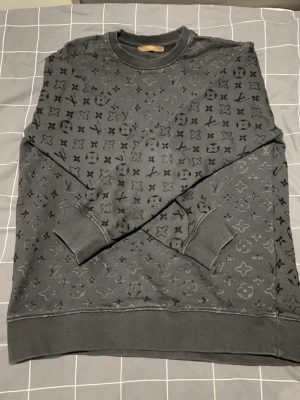 Lv mocka sweatshirt  - Säljer en svart sweatshirt från Louis Vuitton med det klassiska monogrammönstret över hela tröjan. Rund halsringning, ribbade muddar vid ärmslut och nederkant. Perfekt för dig som gillar exklusiva streetwear-plagg. Passar även storlek L!!!