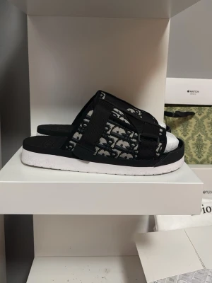 Säljer ett par helt nya inte andvända dior slides perfekta för hemma chill eller under sommaren. - Dessa slides är svart vit grå och blåa med dior mönstring. Det är även ett spänne för att anpassa efter storlek. Skick 10/10 storlek 40-43