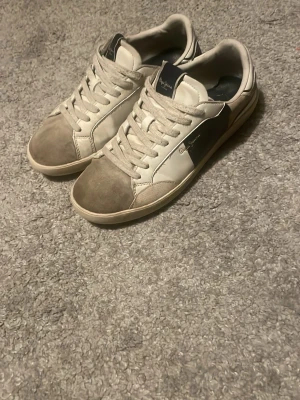 Pepe Jeans  - Snygga sneakers från Pepe Jeans i vitt och grått med mörkblå detalj på sidan och häl. Skorna har klassisk låg modell, snörning och detaljer i mocka och läder. Märket syns på plösen och sidan, samt årtalet 1973 på hälen. Bara höra av sig för fler bilder och pris kan diskuteras vid snabb affär 