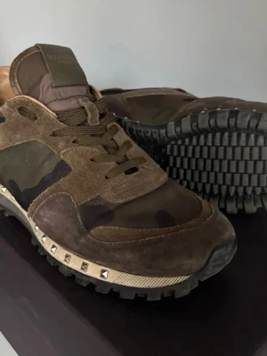 Valentino rockrunners - Snygga sneakers från Valentino i brunt mocka och textil med camomönster och coola silverfärgade nitar runt sulan. Skorna har grov yttersula och klassisk låg siluett. Perfekta för dig som vill sticka ut med en unik och trendig look.