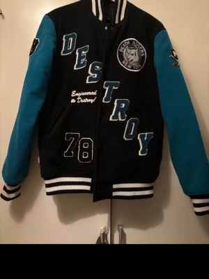 Mishka NYC Retro Destroy RARE!  - Säljer en svart och blå bomberjacka från Destroy med stora bokstäver, broderade detaljer och texten 'Engineered to Destroy!' samt siffran 78. Jackan har vita och svarta muddar och klassisk collegestil. Perfekt för dig som vill sticka ut. 