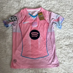 Barça x Nike rosa fotbollströja M - Säljer en FC Barcelona fotbollströja från Nike i rosa och ljusblå toner. Tröjan har korta ärmar, Dri-FIT-material och tydliga detaljer som klubbmärke, Nike-logga och Spotify-sponsor på bröstet. Unik design med mönstrade paneler och Champions League-märke på ärmen. Storlek M!!!
