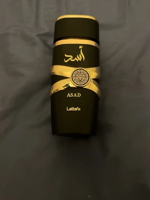 Lattafa Asad parfymflaska svart/guld - Snygg parfymflaska från Lattafa i modellen Asad. Flaskan är svart med eleganta gulddetaljer och arabiska bokstäver på framsidan. Designen är modern och lyxig med en unik form och dekorativt mönster i mitten. Har tyvärr ingen box för parfym men den är oanvänd. Iallafall. 