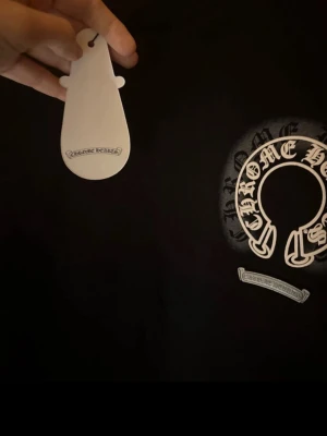 Svart sweatshirt från Chrome Hearts - Säljer en svart sweatshirt från Chrome Hearts med deras ikoniska logga tryckt i vitt på bröstet. Tröjan har rund hals, långa ärmar och ribbade muddar vid ärmslut och nederkant. Perfekt för dig som gillar streetwear och exklusiva märken.