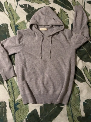 Grå cashmere hoodie från Sayless - Mjuk och stilren grå hoodie från Sayless i cashmere. Klassisk modell med huva och dragsnören, ribbade muddar vid ärmslut och nederkant. Perfekt för dig som gillar en enkel men lyxig look.