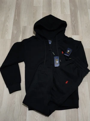 Polo Ralph Lauren Tracksuit svart - Helt ny Polo Ralph Lauren Tracksuit som är svart och har skön och mjuk material och passar för alla väder och årstider. Passar vem som helst och sitter jättefint.