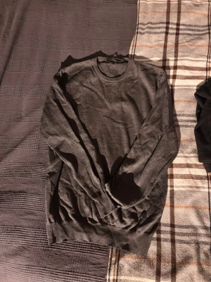 Mörkgrå stickad tröja Bluespheres - Mörkgrå stickad tröja från Bluespheres Original, tillverkad i Italien. Tröjan har rund halsringning, långa ärmar och ribbade muddar vid ärmslut och nederkant. Enkel och stilren design som passar till det mesta.