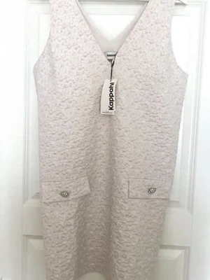 Beige v-ringad klänning KappAhl - Stilren beige kortklänning från KappAhl med v-ringning och ärmlös design. Klänningen har två dekorativa fickor framtill med glittriga knappar och ett diskret strukturmönster i tyget. Perfekt för dig som gillar en enkel men elegant look.