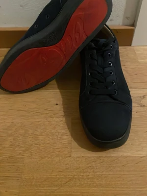 Mörkblå sneakers med röd sula - Snygga mörkblå sneakers från Christian Louboutin med klassisk röd sula. Skorna har ovandel i mocka, svarta skosnören och diskreta detaljer. Perfekta för dig som vill ha en stilren och exklusiv look.