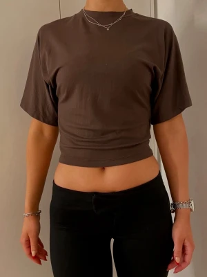 Brun croppad t-shirt - En brun croppad t-shirt med rund hals och korta ärmar. Toppen har en enkel och stilren design som passar perfekt till jeans eller kjol. Tillverkad i mjukt bomullsmaterial för en bekväm känsla. ✨