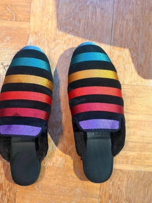 Färgglada handgjorda hums tofflor stl 38 - Ett par färgglada handgjorda tofflor från hums med regnbågsrandigt mönster. Perfekt för att piffa upp vardagen. Är i storlek 38 och är ganska smala. Är aldrig använda. Hämtas på Södermalm i Stockholm eller skickas till dig. Du bestämmer. Maila mig vid frågor. Med vänlig hälsning, Fanny. 