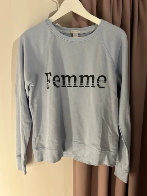 Ljusblå sweatshirt med Femme-tryck - Ljusblå sweatshirt från AMISU med svart text 'Femme' framtill. Tröjan har rund halsringning och långa ärmar. Perfekt för en avslappnad och trendig look. Lite nopprig!!