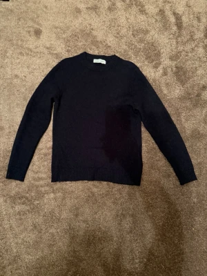Mörkblå stickad tröja Samsøe Samsøe - Mörkblå stickad tröja från Samsøe Samsøe med rund halsringning och ribbade muddar vid ärmslut och nederkant. Klassisk och enkel design som passar perfekt till lager på lager under kyliga dagar. Materialet ser mjukt och bekvämt ut. Storlek M 