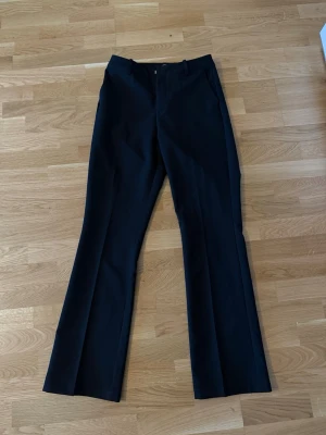 Svarta kostymbyxor från BikBok - Snygga svarta kostymbyxor från BikBok med raka ben och pressveck. Byxorna har fickor i sidorna, hällor för skärp och stängs med dragkedja och knapp. Perfekta för en clean och stilren look.