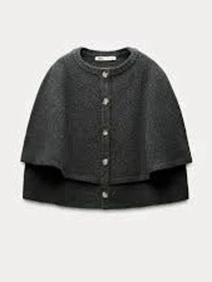 Mörkgrå stickad poncho med knappar - Mysig mörkgrå stickad poncho med ribbad kant och knappar längs framsidan. Ponchon har en rund halsringning och är tillverkad i ett mjukt material som ger en avslappnad look. Perfekt att slänga över en hoodie eller tröja för extra värme.