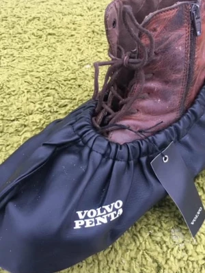 Volvo Penta skoskydd i svart - Säljer ett par svarta skoskydd från Volvo Penta med logga på sidan. Skoskydden är tillverkade i ett tåligt syntetmaterial och har resår runt kanten för att sitta bra över skon. Perfekt när du vill skydda dina skor från smuts och väta.