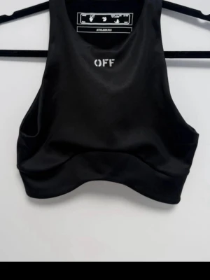 Svart cropped linnetopp Off-White - Sportig svart cropped linnetopp från Off-White med hög halsringning och vit logga framtill. Toppen är ärmlös och har en tight passform i ett stretchigt syntetmaterial, perfekt för träning eller streetwear.