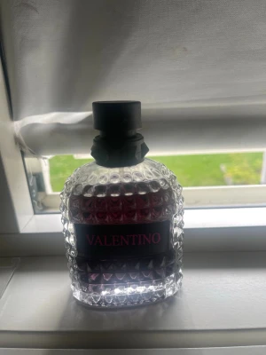 Valentino parfym med nitar (men) - Säljer en lyxig parfym från Valentino i en genomskinlig glasflaska med nitar och svart etikett med rosa text. Flaskan har en unik, kantig form och svart spraymunstycke. Perfekt för dig som gillar exklusiva dofter och snygg design. Pris kan diskuteras vid affär, några sprutor har används