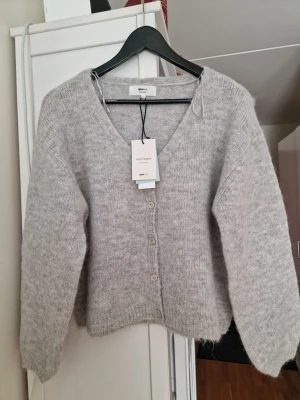 Ljusgrå kofta från Gina Tricot XS - Mysig ljusgrå kofta från Gina Tricot i ullblandning. Koftan har v-ringning, långa ärmar och stängs med fyra knappar framtill. Perfekt för lager på lager och enkel att matcha med olika outfits. Storlek XS