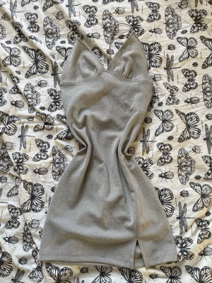 Silver glittrig kort klänning - Snygg silverfärgad kort klänning med glittrigt tyg och smala axelband. Klänningen har en v-ringad front och öppen rygg 