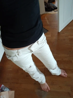 Vita slitna jeans med raka ben - Säljer ett par vita jeans med raka ben och slitningar vid knäna. Jeansen har klassisk femficksdesign och låg midja. Perfekta för en avslappnad och trendig look.