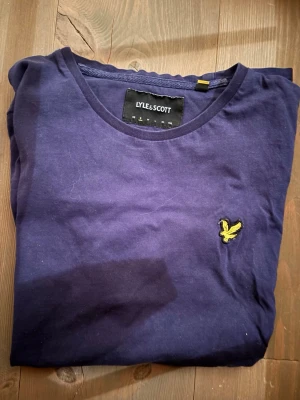 Mörkblå t-shirt från Lyle & Scott - Snygg mörkblå t-shirt från Lyle & Scott med klassisk rund hals och gul logga broderad på bröstet. Tillverkad i mjuk bomull som känns skön mot huden. Perfekt till jeans eller shorts för en clean och enkel stil. Båda säljs tillsammans! T shirten är S och sweatshirt är M