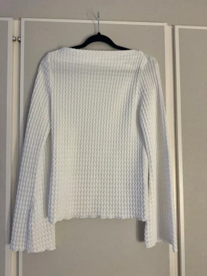 Vit strukturerad långärmad topp - Säljer en vit långärmad topp med vågig, strukturerad yta. Toppen har en rak passform och vida ärmar, vilket ger en trendig och avslappnad look. 