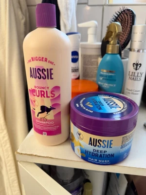 Aussie schampo & hårinpackning - Säljer ett set med Aussie Bouncy Curls schampo i ljusrosa flaska med lila kork och en Aussie Deep Hydration hårinpackning i blå och lila burk. Perfekt för dig som vill ha återfuktat och lockigt hår.