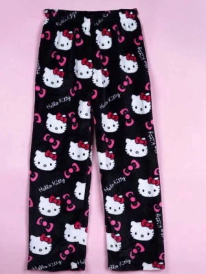 svarta Hello Kitty pyjamasbyxor  - Mysiga pyjamasbyxor med Hello Kitty-motiv på svart bakgrund. Byxorna har elastisk midja och är dekorerade med vita Hello Kitty-ansikten, röda rosetter och rosa detaljer. Perfekt för chillkvällar hemma.