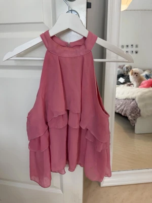 Rosa volang topp med halterneck - Söt rosa topp med halterneck och flera lager volanger. Toppen är ärmlös och har en knapp i nacken för stängning. 🩷