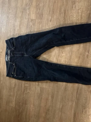 Mörkblå slim fit jeans Dressmann - Snygga mörkblå slim fit jeans från Dressmann med klassisk femficksdesign och kontrastsömmar. Jeansen har en modern passform som sitter tajt längs benen och är perfekta för en stilren look. Tillverkade i ett mjukt och stretchigt denimtyg.