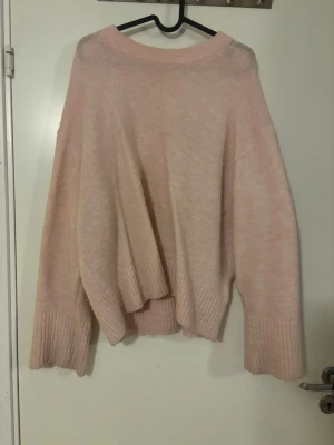 Oversized ljusrosa stickad tröja - Mysig oversized stickad tröja i ljusrosa med breda ribbade muddar vid ärmslut och nederkant. Tröjan har en avslappnad passform och rund halsringning. Superfin färg, tröjan är använd men fortfarande i bra skick.