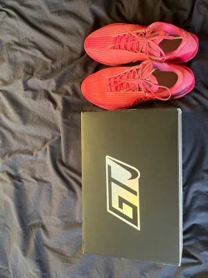 Nike Gt Cut 3 Rob Dillingham  - Säljer ett par Nike Gt Cut 3 Rob dillingham basketskor i en snygg rosa färg med guldfärgade detaljer och svart mönster på sidan. Skorna har en låg profil, snörning och är tillverkade i syntetmaterial med meshpaneler för bra ventilation. Perfekta för dig som vill sticka ut på basketplanen.