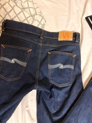 Nudie Jeans Lean Dean Dry Ecru - Säljer ett par mörkblå Lean Dean jeans från Nudie Jeans med klassisk orange söm och vit brodyr på bakfickorna. Modellen är slim fit. (Använda ca 5ggr sen ja köpte de.) kom me prisförslag vetja🤗