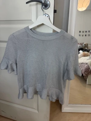 Glittrig silver topp med volang - Säljer en glittrig silverfärgad topp med korta ärmar och volangdetaljer vid ärmslut och nederkant. 🤍