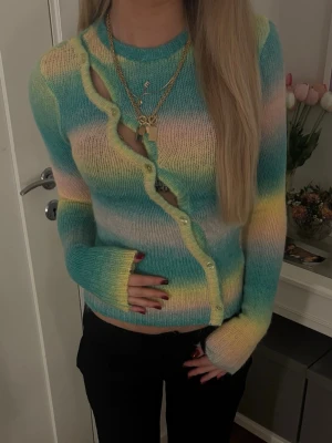 Pastellfärgad stickad kofta - Säljer en stickad kofta i pastellfärger med blått, gult, grönt och rosa. Koftan har långa ärmar, knappar framtill och en mjuk, fluffig känsla. Perfekt för dig som gillar färg och en unik look.
