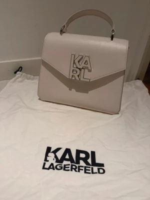 Vit handväska från Karl Lagerfeld - Stilren vit handväska från Karl Lagerfeld. Använt ca 15 gånger. Väldigt fint skick! Köptes för 7000kr väskan finns inte kvar i butik. 