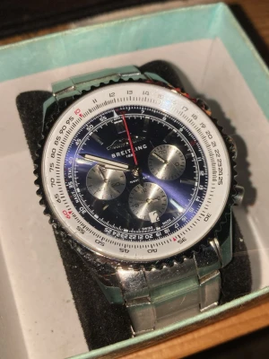 B Navigator klocka, riktigt fin. - Snygg Applelwatch med blå urtavla, tre silverfärgade subdials och röd sekundvisare. Klockan har en robust länkad stålarmband och detaljerad vit bezel med svarta och röda markeringar. Perfekt för dig som gillar klassisk och sportig stil.