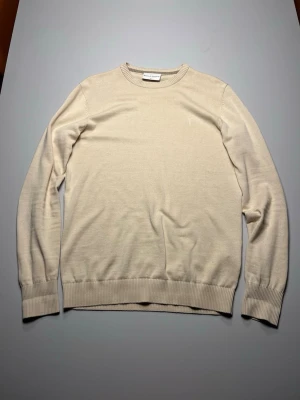 Beige tröja från Bruun & Stengade - Stilren beige tröja från Bruun & Stengade i mjukt material. Tröjan har rund halsringning, långa ärmar och ribbade muddar vid ärmslut och nederkant. Perfekt för en clean och klassisk look.