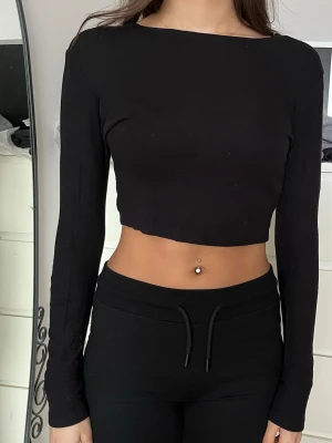 Svart croppad långärmad topp - Säljer en enkel och stilren svart croppad topp med långa ärmar. Toppen har en tight passform och är perfekt att matcha med höga byxor eller kjol. Materialet känns mjukt och stretchigt, vilket gör den bekväm att bära.